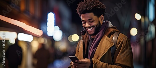 An African American man is using his phone on a city street at night while looking away photo