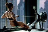 Fitness girl workout on indoor rower at the gym, doing exercises on rowing machine near the window, view of skyscrapers in the background, woman exercising in fitness club
