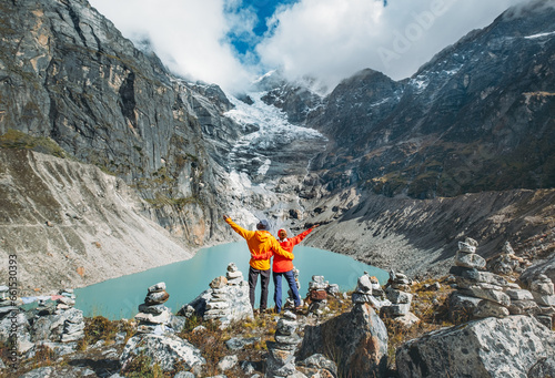 Couple trekkers dressed bright jackets on the rock enjoying a glacier falling in high altitude Sabai Tso glacial lake cca 4350m. Makalu Barun National Park, Mera peak climbing route, Nepal. photo