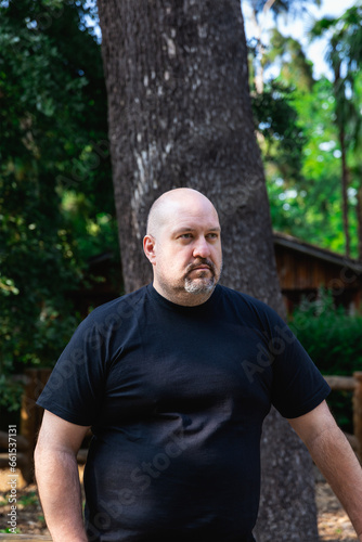 Portrait of a bald mature man with goatee very serious in a park. Outdoor vertical portrait in natural light.