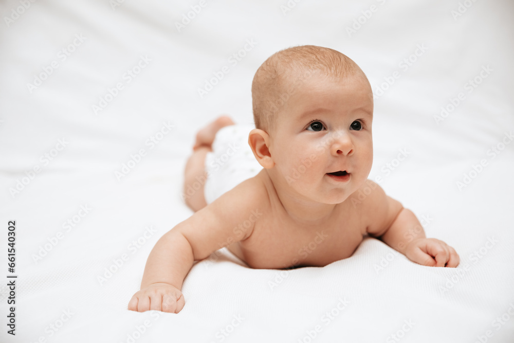 A surprised newborn baby in a diaper is lying on a white blanket and looking. A surprised newborn baby in a diaper is lying on a white blanket and looking.