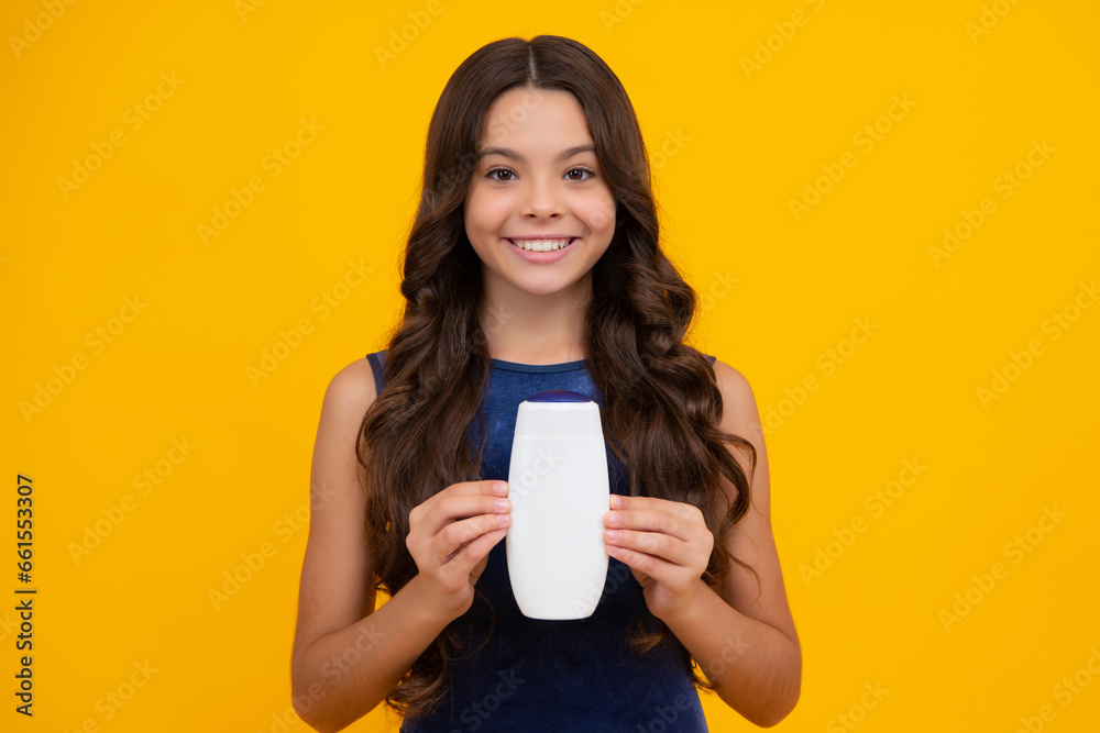 Teen child girl with shampoo bottle or shower gel isolated on yellow background. Kids hair cosmetic product. Happy girl face, positive and smiling emotions. Teen child girl with shampoo bottle or shower gel isolated on yellow background. Kids hair cosmetic product. Happy girl face, positive and smiling emotions.