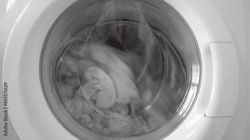 White linen during washing or rinsing rotates in the drum of a home washing machine White linen during washing or rinsing rotates in the drum of a home washing machine