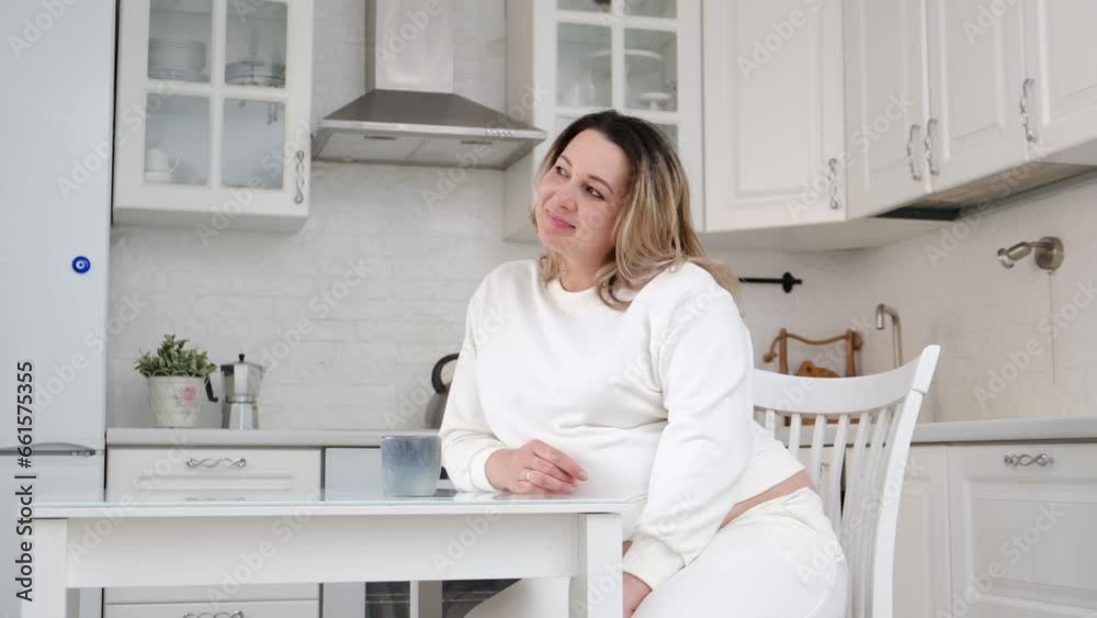 A pretty pergnant woman is drinking tea and sitting at table kitchen. Light background. A pretty pergnant woman is drinking tea and sitting at table kitchen. Light background.