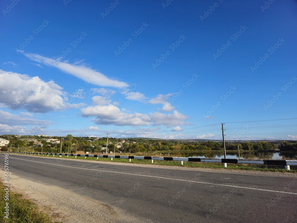 Naklejka premium A road with a body of water and a blue sky with clouds