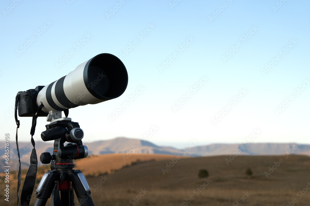 Shooting a distant object with a long lens. Camera on a tripod against the background of mountainous terrain at dawn. Copy space.