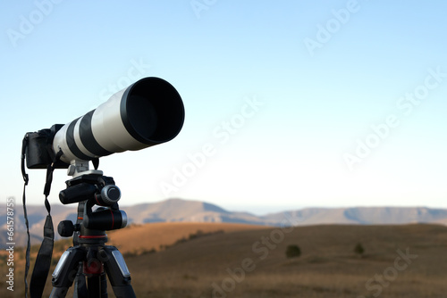 Shooting a distant object with a long lens. Camera on a tripod against the background of mountainous terrain at dawn. Copy space.