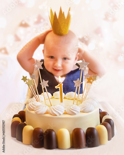 Happy cute kid (1-year-old) with delicious birthday cake (sweets with candles of number one, decoration). Little boy wearing crown. Celebrating child's first year birthday. photo