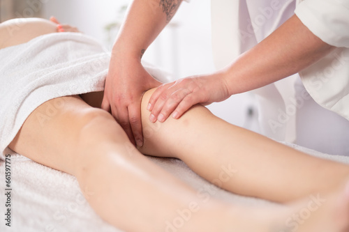 Crop masseuse massaging knee of woman carrying baby
