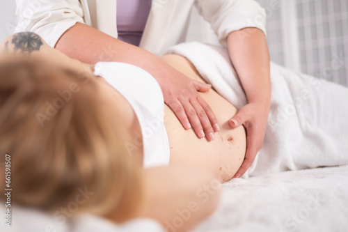Faceless masseuse touching stomach of pregnant anonymous lady