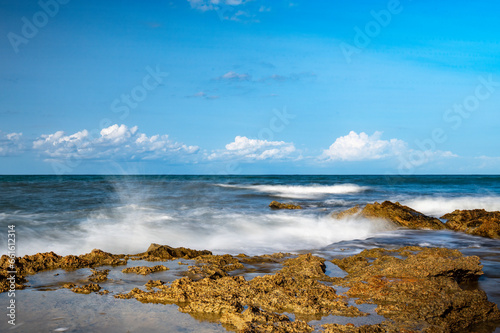 Sea waves break on the stone coast and foam between the rocks.