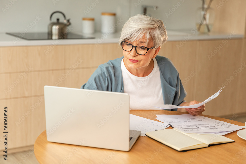 Middle aged senior woman sit with laptop and paper document, Pensive older mature lady reading paper bill pay online at home managing bank finances calculating taxes planning loan debt pension payment - obrazy, fototapety, plakaty 