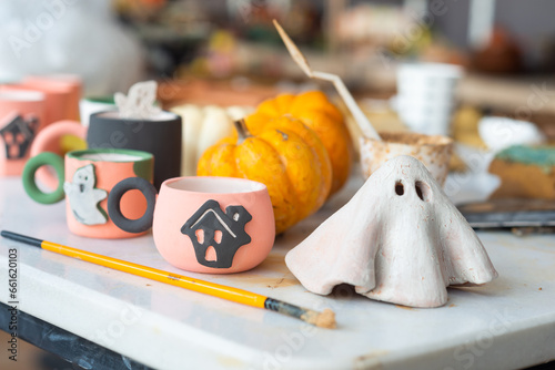 Table cluttered with various unfinished Halloween crafts at a ceramics, pottery studio with tools, brushes, unfinished objects in the making in the background