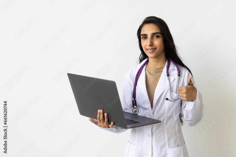 Cheerful young indian woman medical worker in uniform works at computer isolated on white background. Cheerful young indian woman medical worker in uniform works at computer isolated on white background.