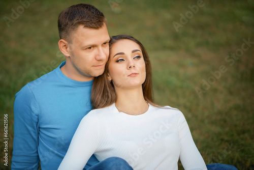 Stylish white man without eyeglasses hugging stylish woman looking at camera on green