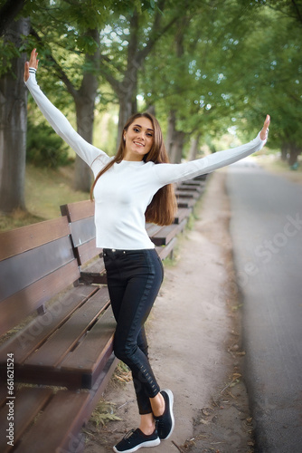 A 25-year-old girl, wearing a white sweater and black jeans, walks in the park and enjoys life.
