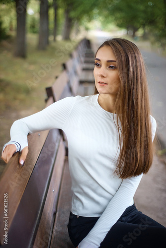 A girl with long hair is walking in the park and sat down on a bench. She's happy with her life