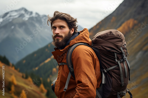 a bearded man with a backpack on his back stands against the background of mountains.