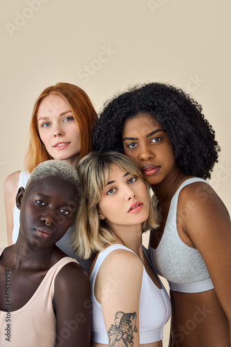 Cool fashion gen z girls in underwear looking at camera, beauty portrait. Four confident diverse young women, multicultural ladies international models bonding isolated on beige background. Vertical