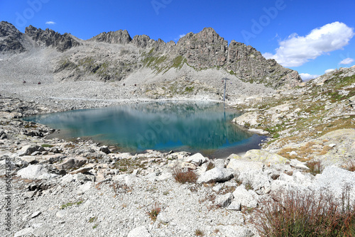 An Alpine haven with a crystal-blue lake, nestled near the Adamello Glacier in the Italian Alps, under a brilliant sunny sky