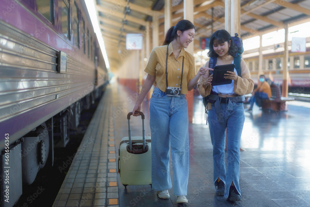 Two Asian female tourists are checking their travel plans on a tablet after getting off a train.