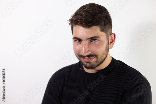 portrait d'un beau jeune homme souriant, brun et barbu, portant un pull-over noir, sur fond blanc. © Tof - Photographie