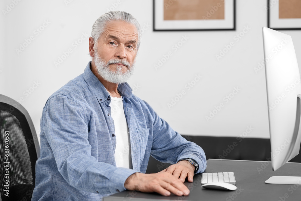 Handsome senior man working on computer at table in office. Space for text
