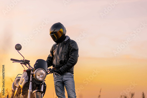 motorcyclist in a helmet and leather jacket at sunset with a classic motorcycle. Moto life concept