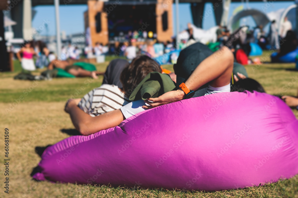 Crowded open air festival concert with musicians band on stage, rock show performance, with concert-goers attendees on beanbags, audience sitting on bean bag chair on a grass lawn on summer festival