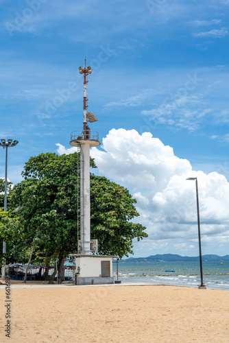 Warning tower with solar panels on the shore of a tropical sea in sunny weather against a background of blue sky with white clouds.