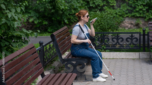 A blind pregnant woman sits on a bench and communicates on a smartphone. 