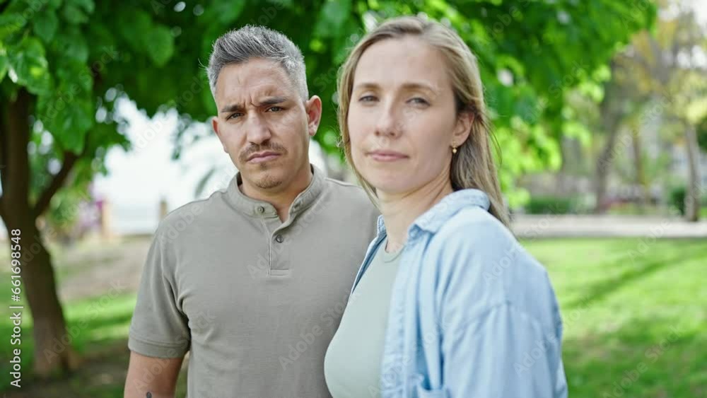 Man and woman couple standing together with serious face at park Man and woman couple standing together with serious face at park