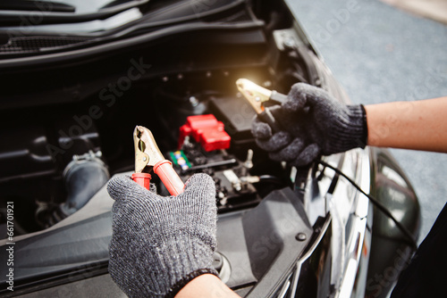 Close-up hand auto mechanic using connect jumper cables on terminal dead battery for jump-start or check car battery fail problem to change repairing and fix car and maintenance servicing.