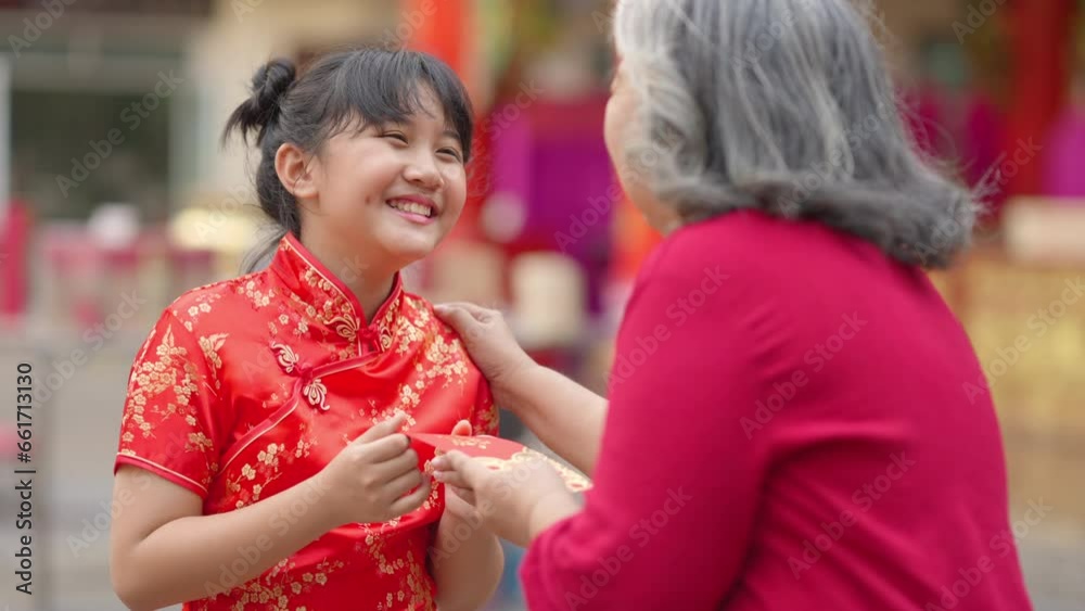 4K Happy Asian family grandmother giving red envelope contained money gift with blessing to little grandchild girl in Chinese red dress. Chinese lunar new year festival and holiday celebration concept