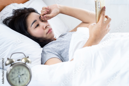 Asian woman rubbing her itchy and tired eye watching too much on mobile phone screen late at night in bed photo