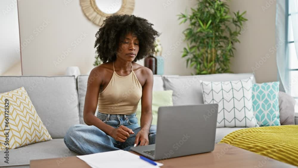 African american woman doing online yoga exercise sitting on sofa at home