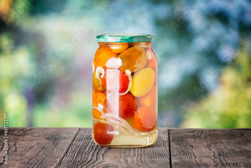 Pickled tomatoes in a glass jar on a wooden rustic table on a color background