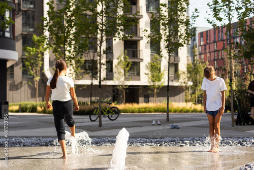 Happy teenage girl dancing in a fountain in a city park on a hot summer day.