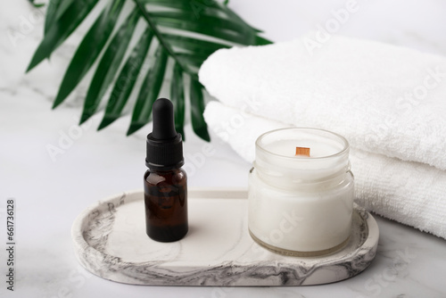 aromatic candle with oil serum in the bathroom on a marble tray with towels, moisturizing facial skin, natural cosmetics