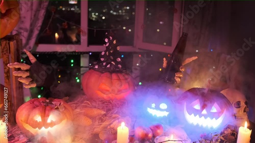 Creepy jack o'lantern with witch hat holding beer bottle and calls to spooky Halloween party with decorations of autumn dry leaves, candles, flickering garlands. photo