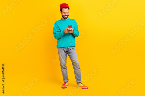 Full length photo of satisfied man dressed turquoise pullover look at smartphone read notification isolated on yellow color background