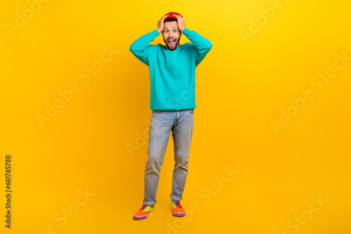Full length photo of speechless crazy man dressed turquoise pullover holding arms on head screaming isolated on yellow color background