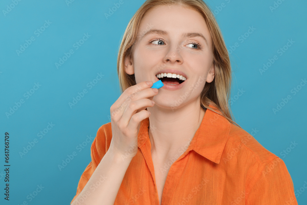 Happy young woman putting bubble gum into mouth on light blue background Happy young woman putting bubble gum into mouth on light blue background