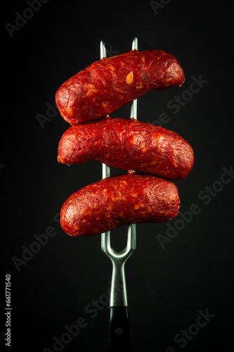 Fried Bavarian meat sausages on a fork. Tasty snack concept for hotel or restaurant on black background