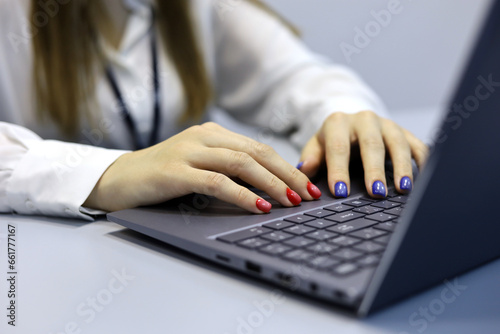 Female hands on laptop at desk. Woman with manicure types on notebook keyboard, nails with manicure of red and blue colors