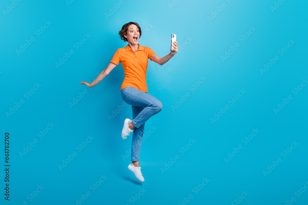 Full size photo of impressed excited girl dressed stylish polo denim trousers flying look at smartphone isolated on blue color background