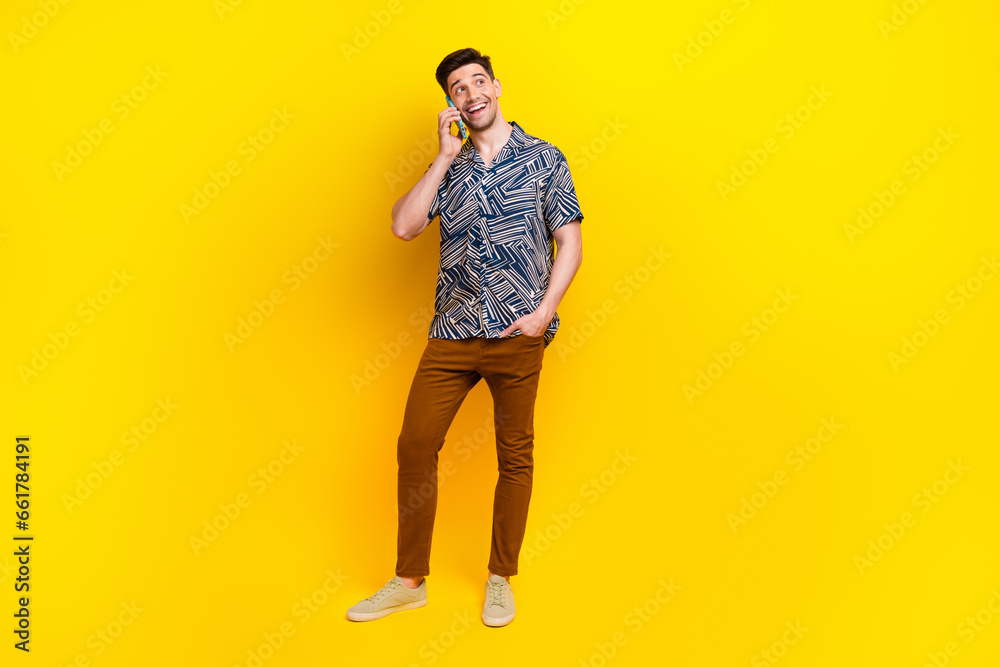 Fototapeta premium Full size photo of friendly guy wear stylish shirt trousers talk on smartphone look empty space isolated on yellow color background