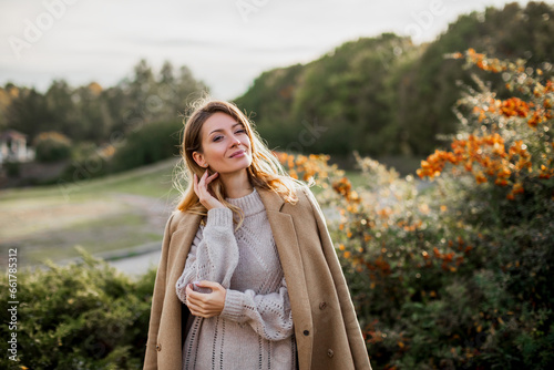 Beautiful portrait of a Caucasian girl in an autumn coat walks on a warm sunny day in the autumn park. Happy young woman enjoying golden autumn. autumn leaves.    