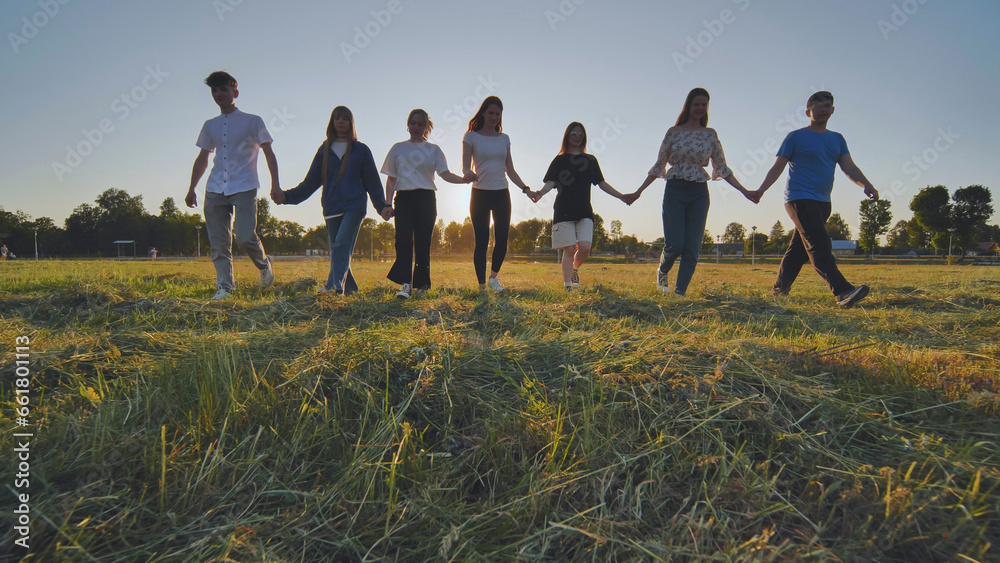 Friends at sunset holding hands walking against the backdrop of the setting sun. Friends at sunset holding hands walking against the backdrop of the setting sun.