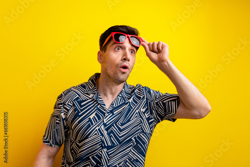 Portrait of impressed speechless person arm touch sunglass look empty space isolated on yellow color background